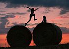 Zwei Geschwister spielen vor dem farbenprächtigen Abendhimmel auf Strohrollen, die auf einem abgeernteten Getreidefeld im brandenburgischen Petersdorf liegen. picture alliance / dpa; © dpa