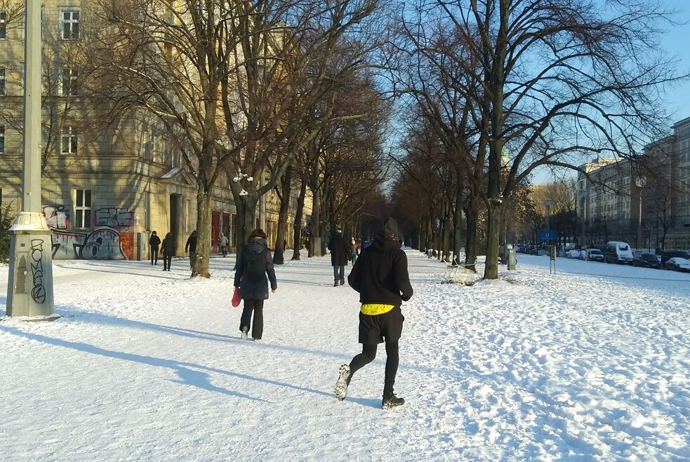 Spaziergänger*innen und ein Jogger auf der Karl-Marx-Allee, als im Februar kurzzeitig Schnee fiel