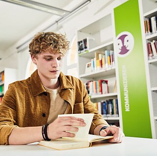 Ein junger Mann liest liest ein Buch in der Bibliothek 