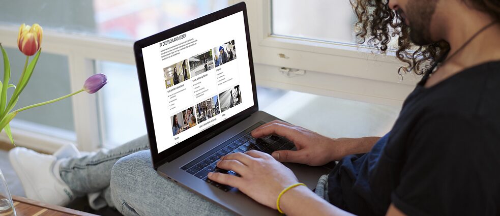 Man browses on page „Mein Weg nach Deutschland“ on his laptop