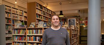 Ein Mann steht lächelnd vor mehreren Bücherregalen.