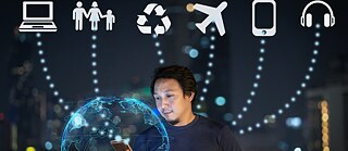 Man with smartphone standing in front of a hologram, in the background are different symbols such as a plane or a computer..