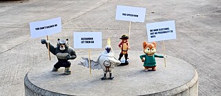 Kleine Spielfiguren halten Protestplakate mit Aufschrift hoch.