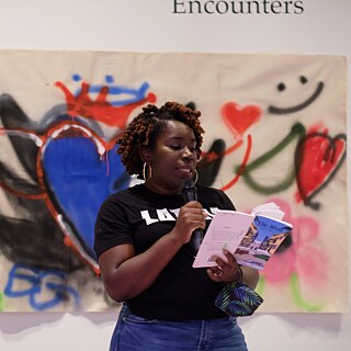 A woman with a microphone reading a book aloud to an audience