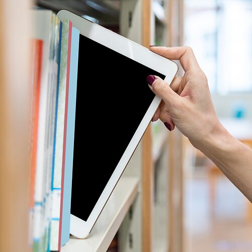 La main d'une femme prend une tablette numérique dans une étagère de bibliothèque.