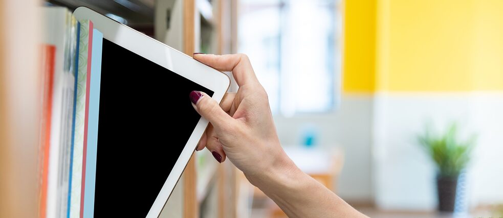 La main d'une femme prend une tablette numérique dans une étagère de bibliothèque.