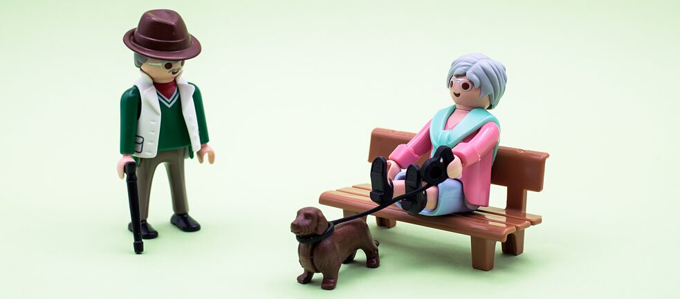 Eine Spielfigur geht spazieren, eine andere sitzt mit ihrem Hund an der Leine auf einer Parkbank