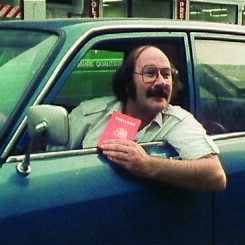 Foto von Antonio Skármeta, der auf dem Sitz eines Autofahrers sitzt. Er lehnt sich aus dem Fenster und hält einen Pass in der Hand.
