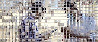 The figures of two men are seen behind a surface partly filled with of wooden blocks.