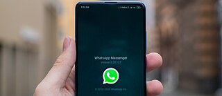 Eine Hand hält ein Handy mit WhatsApp auf dem Screen