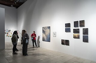 Photographs in different sizes hanging in an exhibition hall. A group of visitors are looking at the works.