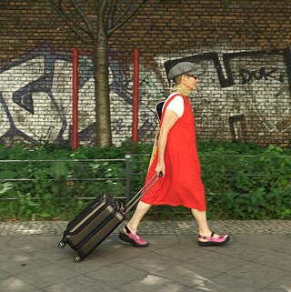 Ella Dreyfus walks along a footpath pulling a wheeled suitcase. 