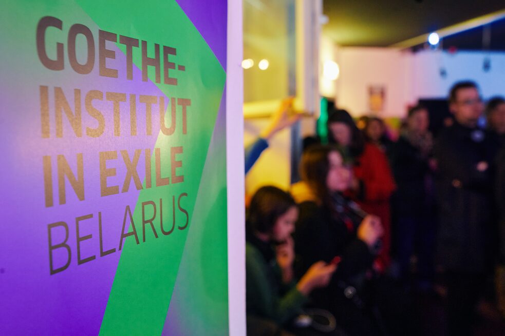 Lila-grünes Roll-Up mit dem Schriftzug Goethe-Institut in Exile Belarus mit Publikum im Hintergrund