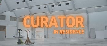 The picture shows an empty factory building with the words ‘Curator in residence’ on it.
