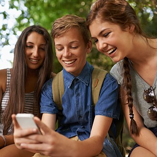 Three young people look at a smartphone and laugh.