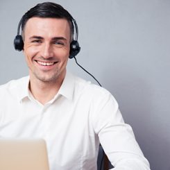 A smiling man with headphones looking up from his laptop.
