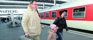 Eine Familie geht auf einem Bahnsteig entlang, im Hintergrund steht ein Zug.