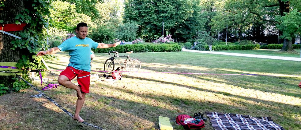 Ein Mann balanciert auf einer Slackline in einem Park.