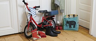 In one room there is a red children's bicycle, children's rubber boots and shoes of an adult.