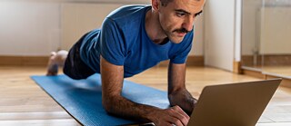 Man doing a plank and using laptop at home
