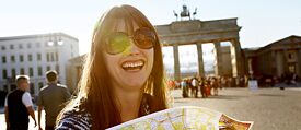 Een jonge, lachende vrouw staat voor de Brandenburger Tor in Berlijn. 