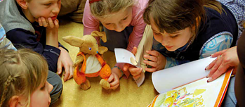 Kinder schauen sich zusammen mit der Hans-Hase-Handpuppe ein Buch an. 