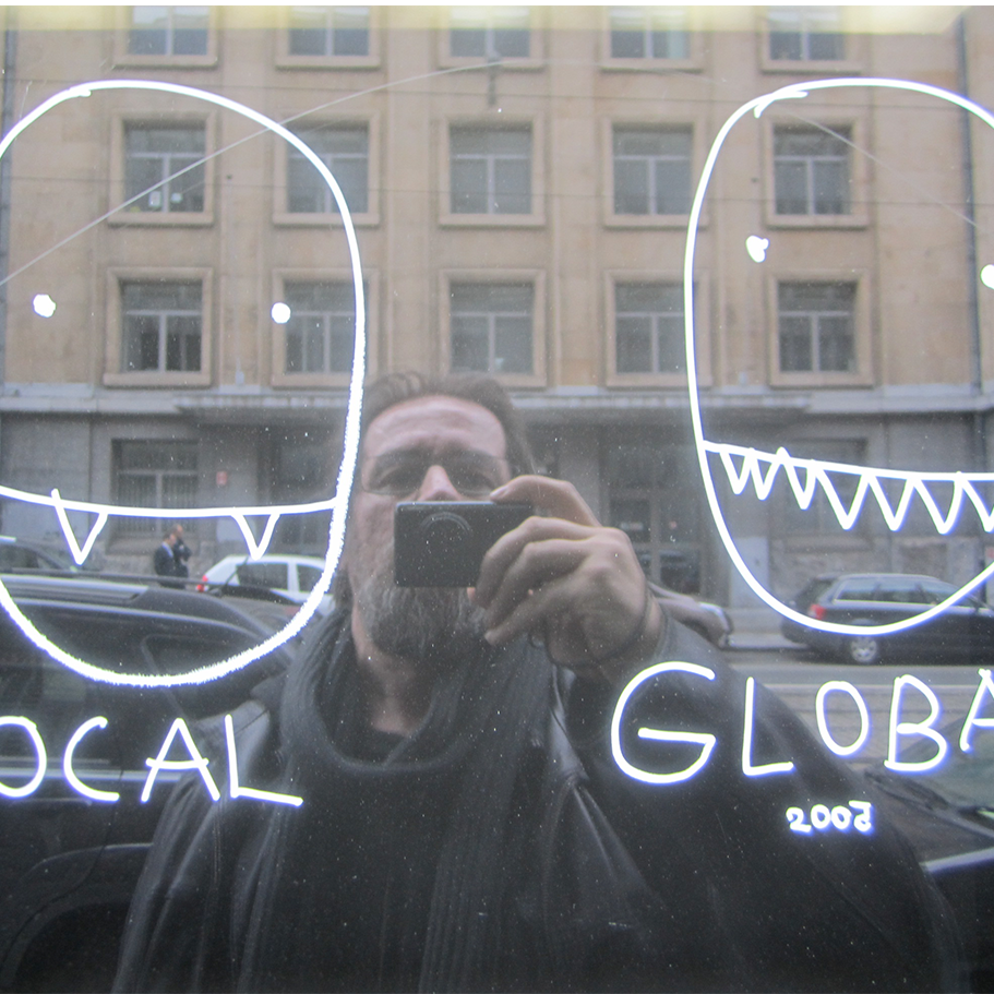 Дан Пержовски си прави селфи пред прозорец с рефлексни стъкла. На прозореца отляво и отдясно са скицирани две глави с надписите local и global
