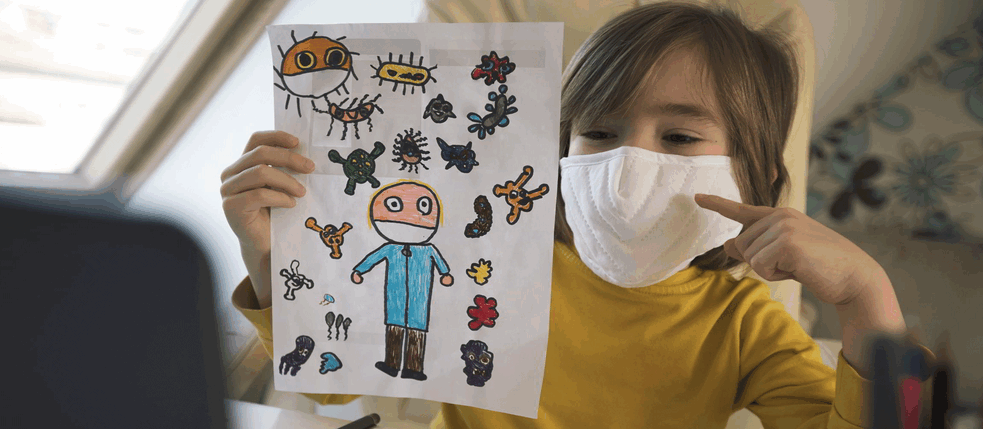 Ein Kind mit Mund-Nasen-Schutz zeigt eine Zeichnung.