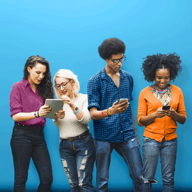 Vor einem blauen Hintergrund schauen 4 junge Menschen gemeinsam auf ihre Handys und Tabltes
