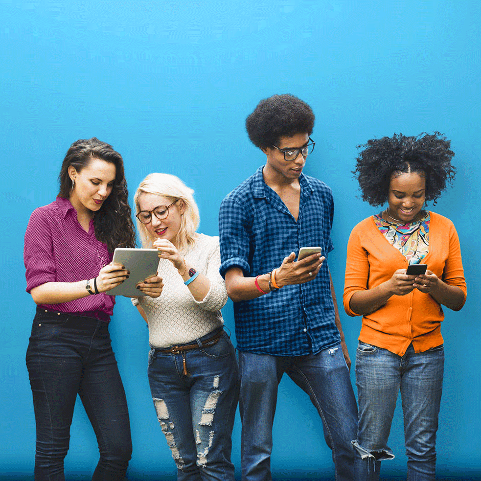 Vor einem blauen Hintergrund schauen 4 junge Menschen gemeinsam auf ihre Handys und Tablets 