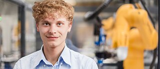 Ein junger Mann mit einer Maschine im Hintergrund.