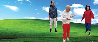 Das Bild zeigt den Windows-Hintergrund: ein grünes Feld mit einem Hügel und ein blauer Himmel mit Wolken. Zwei Frauen und ein Mann in Sportkleidung scheinen über dem Feld zu schweben und starren jeweils in verschiedene Richtungen.