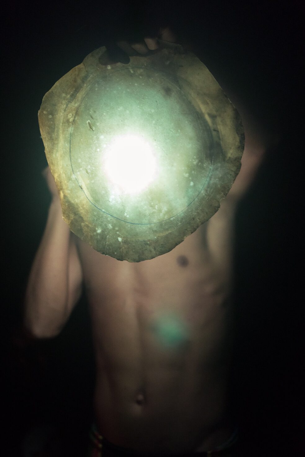 A young man inspects the skin of a javelin, which is being dried to be used as a tambourine.