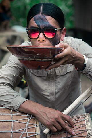 2017. Celso Aranda bebe chicha no terceiro dia da festa Uyantza Raymi. A chicha é uma bebida tradicional feita de iúca. No preparo da chicha, a raiz é cozida por várias horas, depois espremida para formar um tipo de purê, mastigada e cuspida. Por fim, a bebida é derramada em potes de argila cobertos de folhas para fermentação. A chicha é preparada exclusivamente por mulheres. 