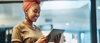 Eine junge Frau blickt auf ein Tablet und lächelt.