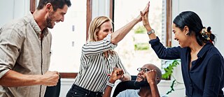 Eine Gruppe junger Leute in einem Büro jubeln und klatschen sich ab.