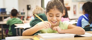A happy little girl sits in front of a textbook in the classroom.