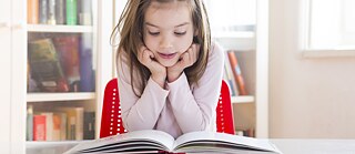 Ein kleines Mädchen brlickt gespannt in ein Buch, das vor ihr liegt.