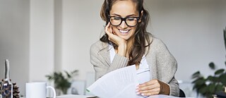 A young woman is sitting at a table, leafing through a thick book.