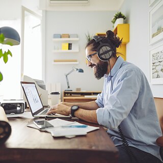 Ein junger Mann sitzt in einem hellen, freundlichen Büro am Schreibtisch und tippt in ein Laptop.