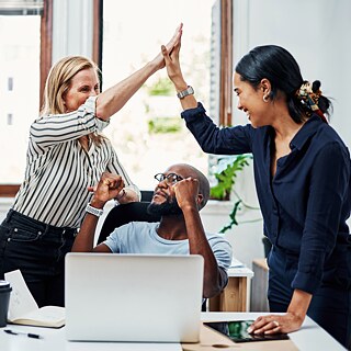 A group of young people in an office are cheering and exchanging high-fives.