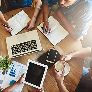 View from above of young people in a café. A laptop, smartphone and notebooks are on the table.