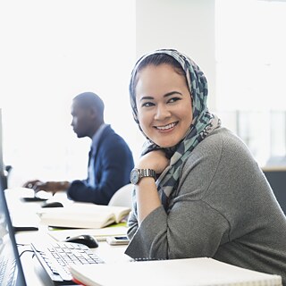 Eine junge Frau sitzt in einer Bibliothek vor dem Computer.