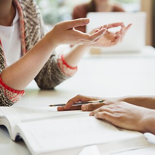 Nahaufnahme von Händen zweier Studierender. Vor ihnen liegen aufgeschlagene Bücher.