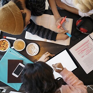 تلميذ يجلس مع معلمته أمام طاولة ويقوم بكتابة نص بقلم فسفوري.