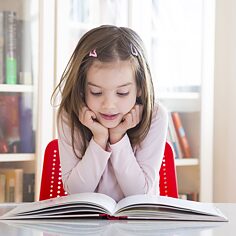 Ein kleines Mädchen blickt gespannt in ein Buch, das vor ihr liegt.