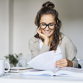 A young woman is sitting at a table, leafing through a thick book.