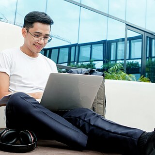 Junger Mann sitzt mit einem Laptop vor einem Firmengebäude