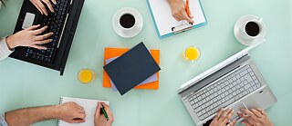A table with laptops, books and coffee cups and arms