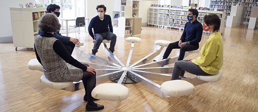 Five people sit on a circular seat in a library